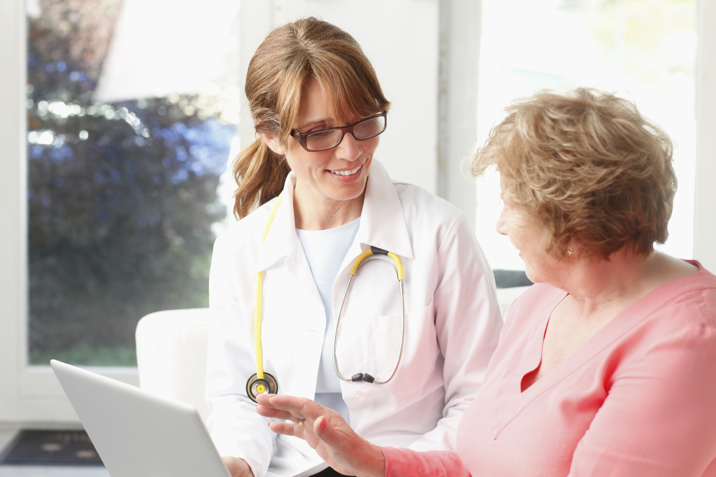 Close-up of happy female doctor talking with senior patient at clinic.